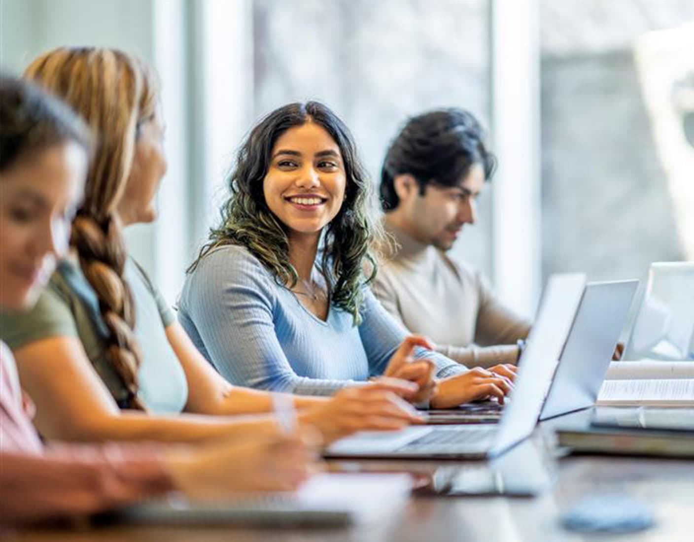 A diverse group of students collaborates at a table, each focused on their laptops during a study session.